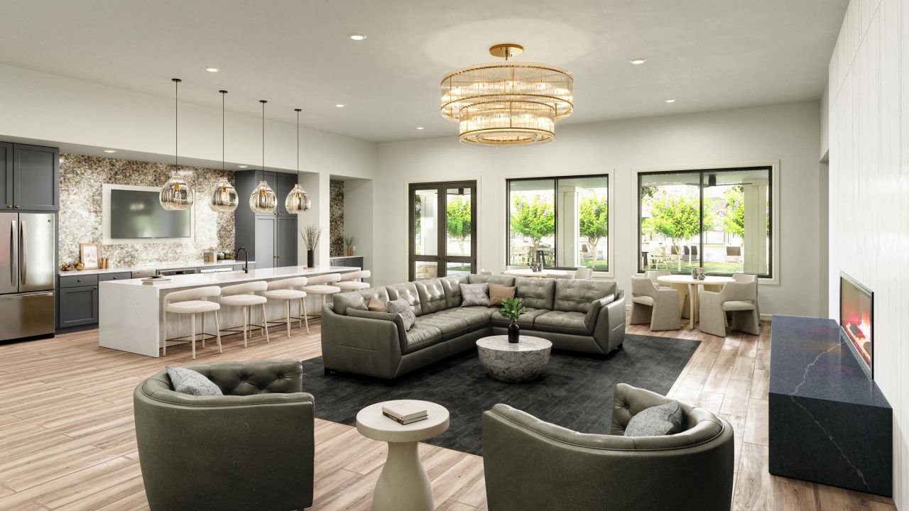 The interior of the clubroom at Artesia at Medina Valley, featuring a spacious living area, a luxurious chandelier, and an open kitchen.